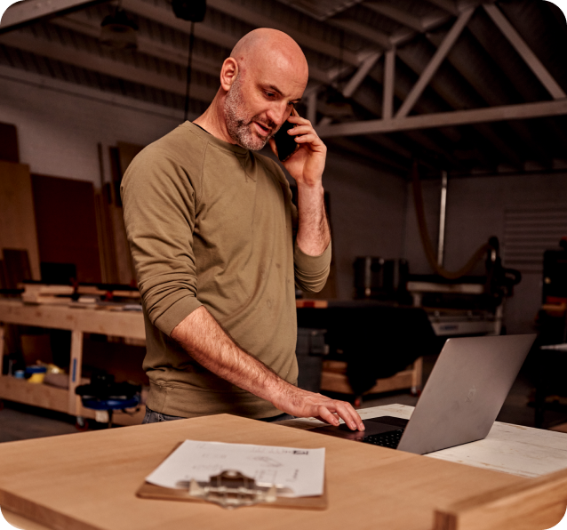 A worker chatting on the phone while looking at a laptop